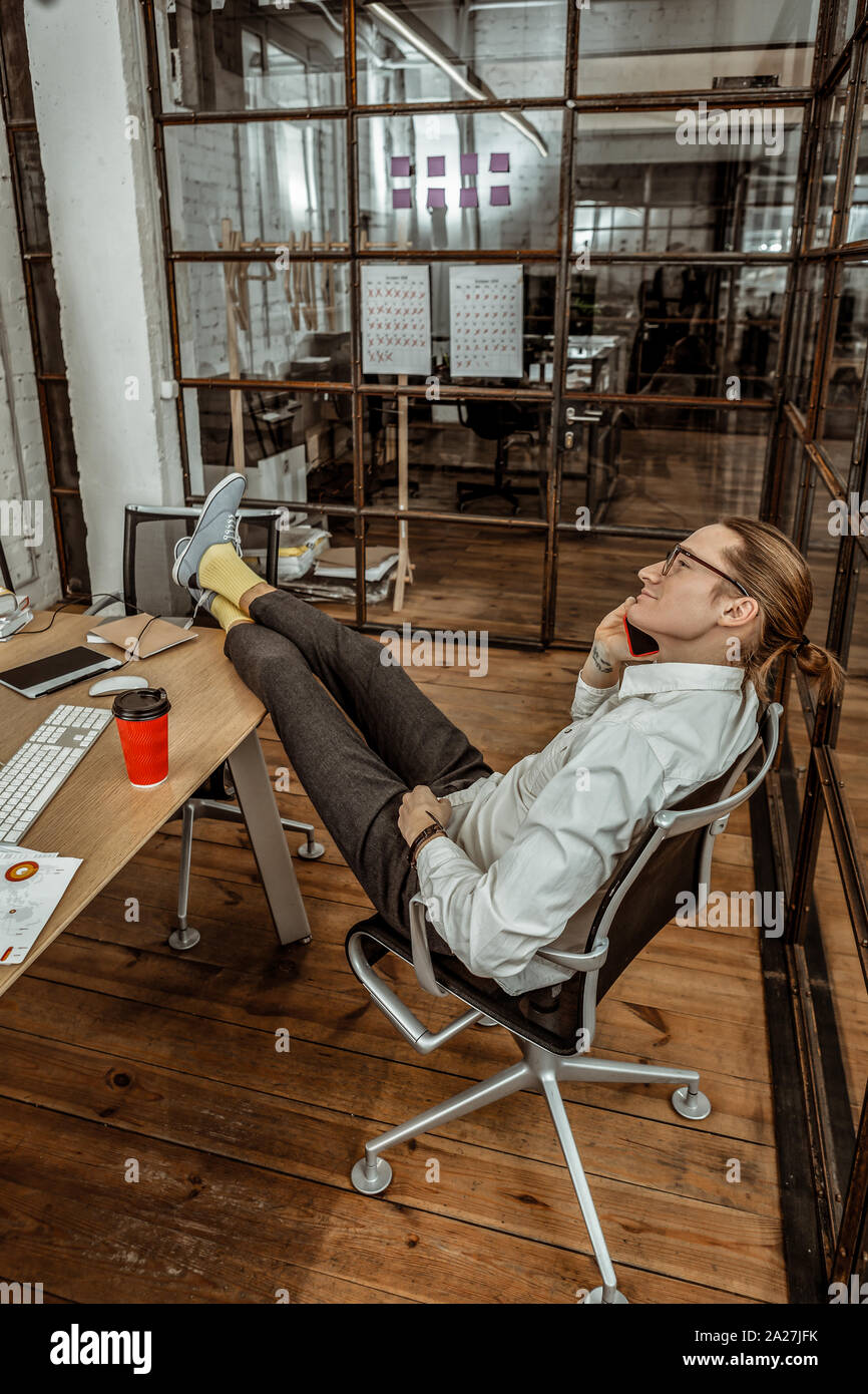 Having break. Cheerful young man putting feet on table while enjoying