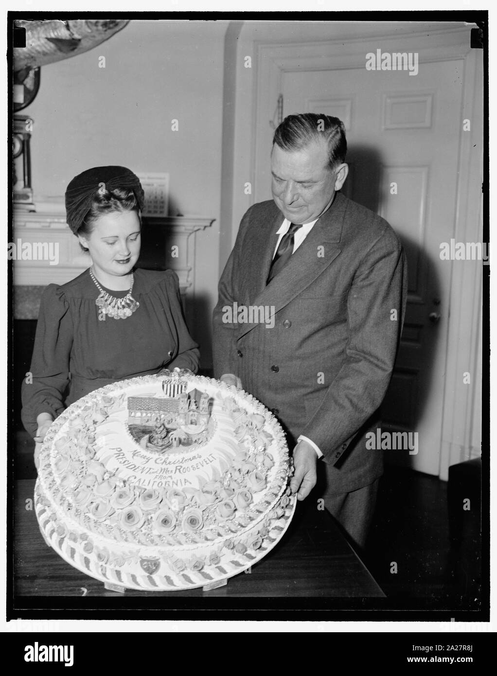 President gets Xmas fruit cake. Washington, D.C., Dec. 19. Brig. Gen. Edwin Watson, a Presidential Secretary, accepting for President Roosevelt a fruit cake from Miss Mildred Cook, Secretary to Rep. A.J. Elliott of California. The cake is a gift from W.C. Baker of Ojai, Calif., who has baked cakes for the White House for the last 17 years Stock Photo