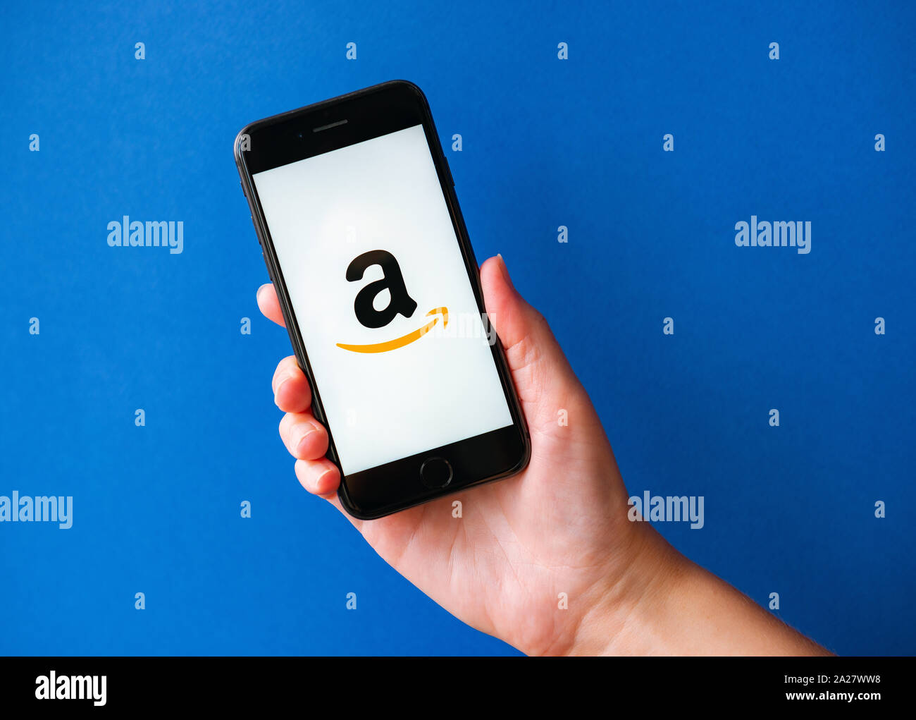 Kyiv, Ukraine - October 1, 2019: Studio shot of hand holding Apple iPhone 8 with Amazon logotype on a screen. Isolated on a blue paper background. Stock Photo