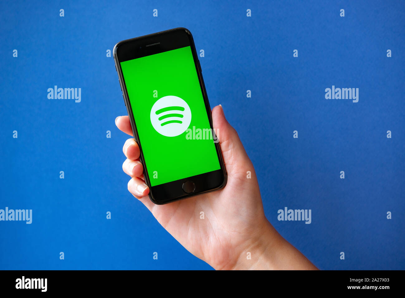 Kyiv, Ukraine - October 1, 2019: Studio shot of hand holding Apple iPhone 8 with Spotify logotype on a screen. Isolated on a blue paper background. Stock Photo