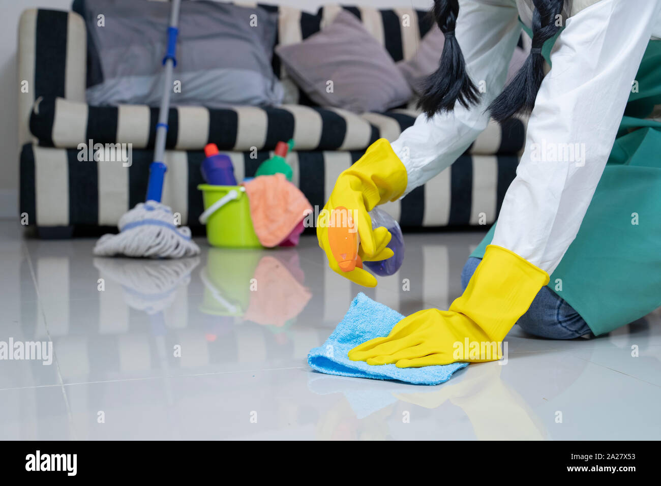 Asian woman in green overalls and yellow, rubber gloves dusting a floor. Stock Photo