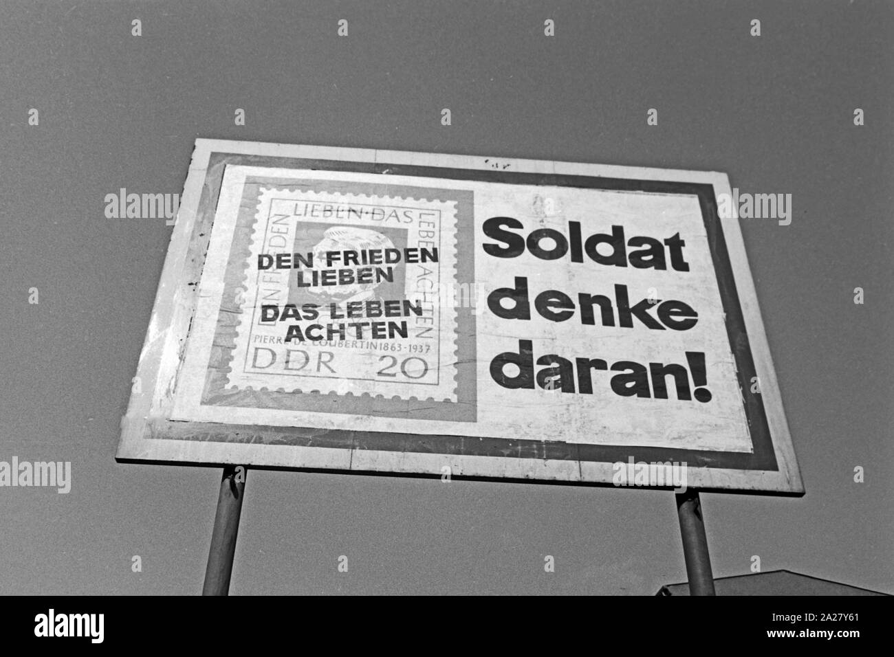 DDR Propaganda Schild mit einer Briefmarke mit Pierre de Coubertin und dem Aufdruck 'Den Frieden lieben - Das Leben achten' in Berlin, Deutschland 1963. GDR propaganda with a stamp of Pierre de Coubertin at Berlin, Germany 1963. Stock Photo