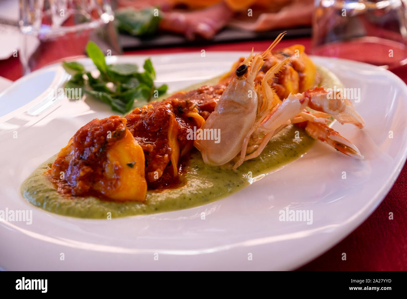 Layered stack of delicious langoustine ravioli on a green herb sauce base.  Drizzled over the top is a rich tomato sauce set off on a white plate Stock  Photo - Alamy