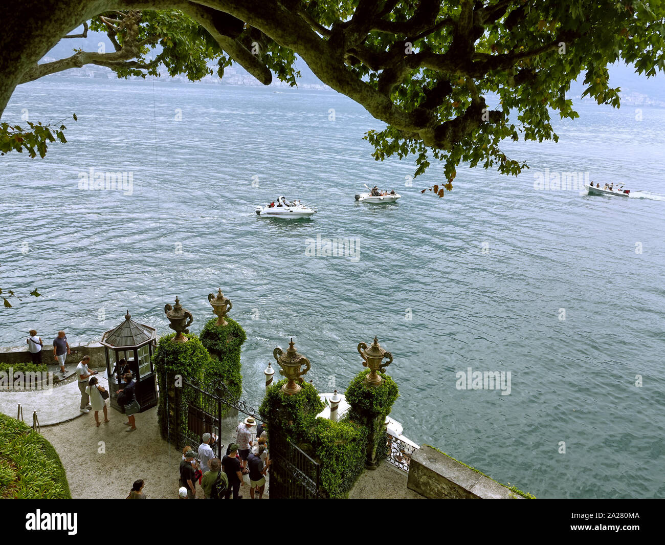 Lake Como, Lombardy, Italy. Tourists wait for their  ferry transport whilst a powerboat speeds by The gardens of Villa del Balbianello,  near Lenno, L Stock Photo