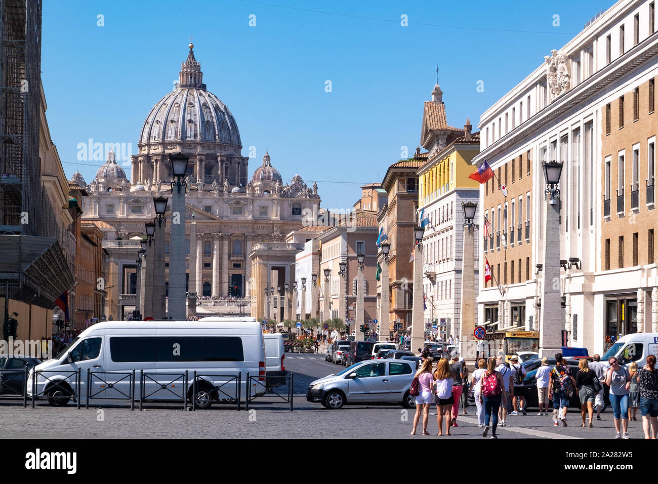 Busy street of traffic and vibrant tourists approaching the St Peters Basilica of Vatican City, Rome in the bright sunlight. Stock Photo
