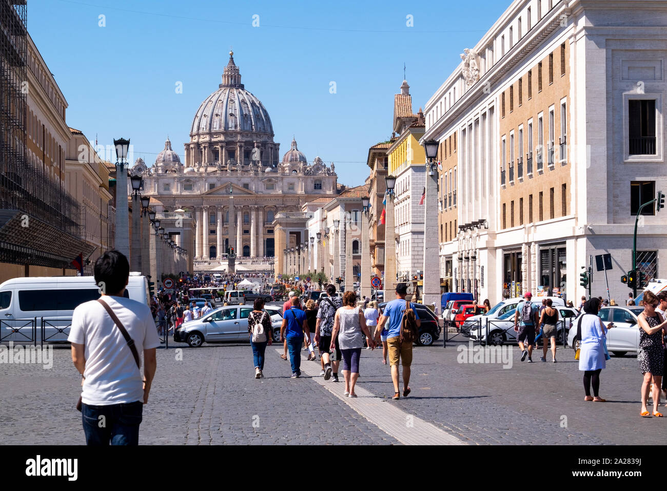 Busy street of traffic and vibrant tourists approaching the St Peters Basilica of Vatican City, Rome in the bright sunlight. Stock Photo