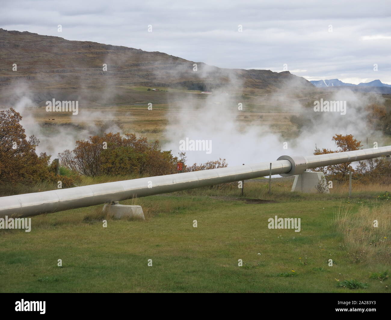 Green energy in Iceland: steam rises from the hot springs at Deildartunguhver and a distribution pipe takes the hot water for central heating. Stock Photo