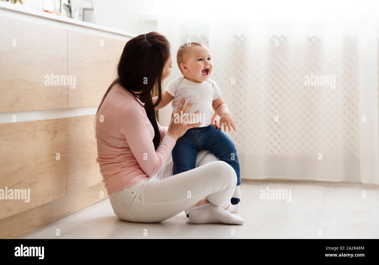 Adorable baby playing with mom, sitting on floor in kitchen Stock Photo ...