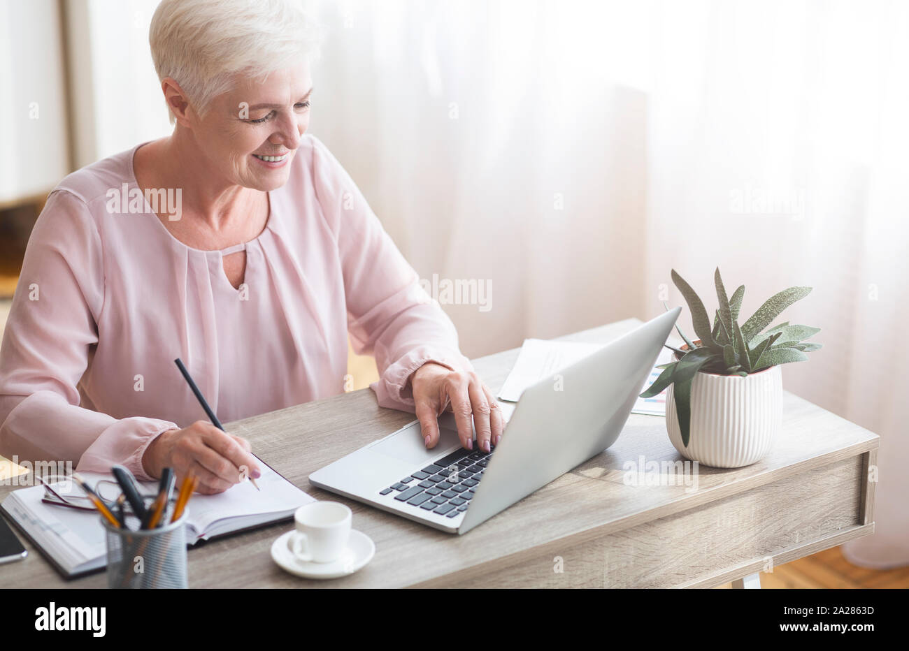 Top view of mature working lady making notes, using laptop Stock Photo