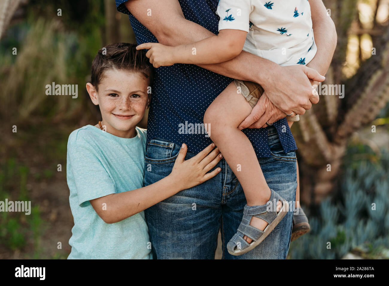 Mid view of elementary age boy hugging father and brother and smiling Stock Photo