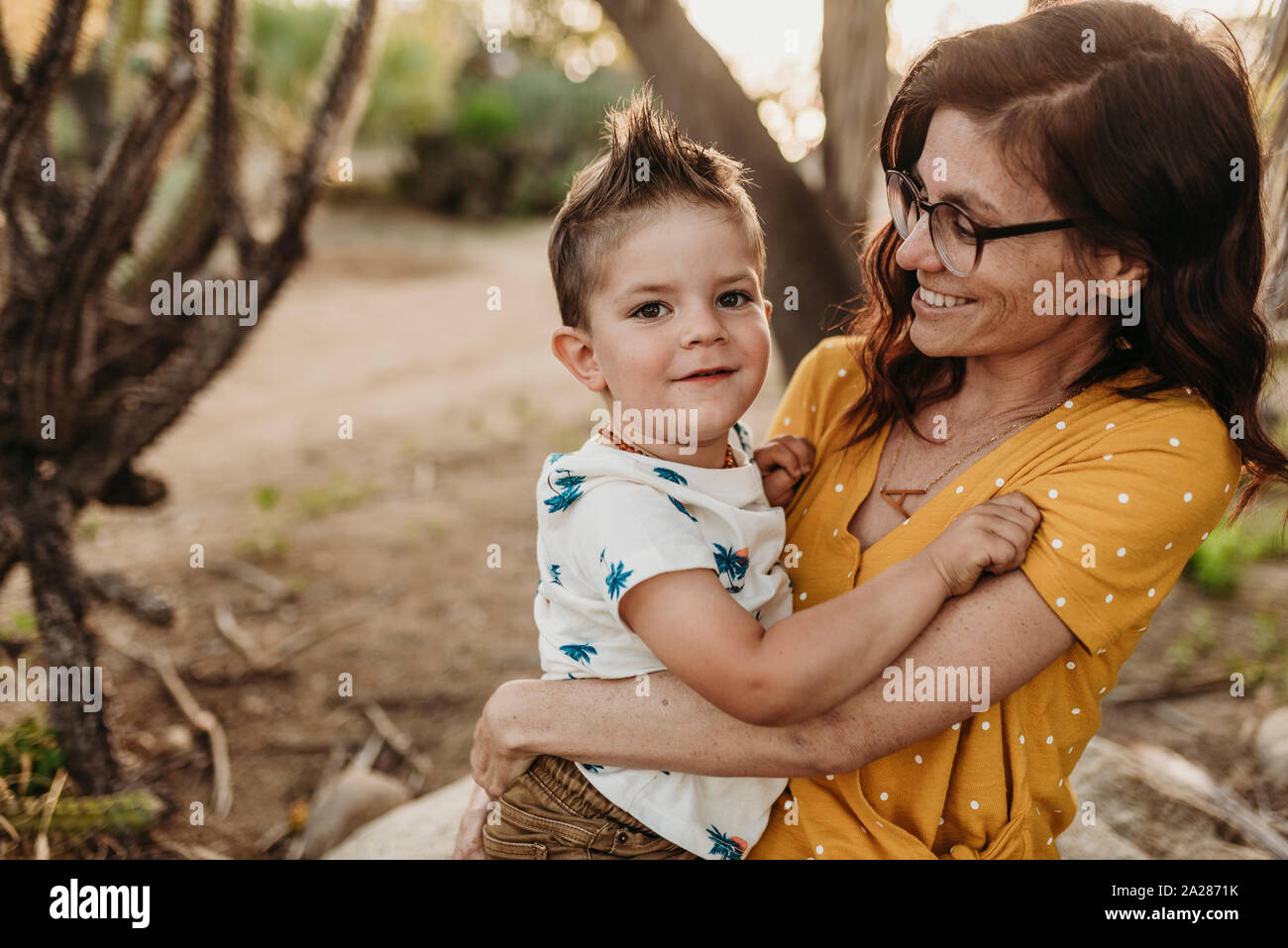 Mother holding young son and smiling in backlit cactus garden Stock Photo