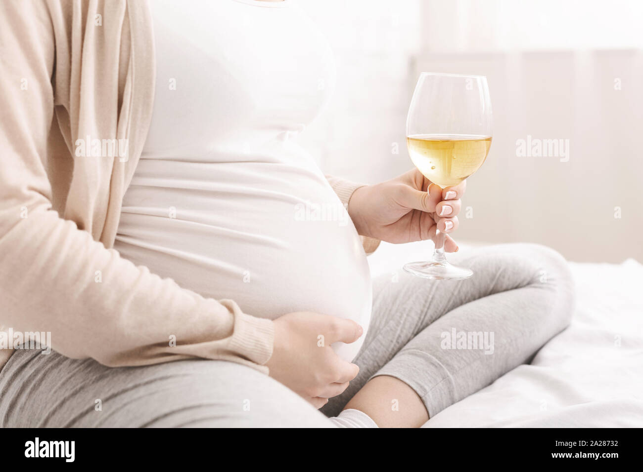 Pregnant woman in kitchen with glass of red wine smiling Stock Photo