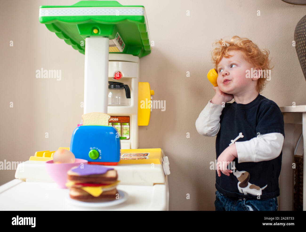 Toddler boy answering phone in his play kitchen with cute expression Stock Photo