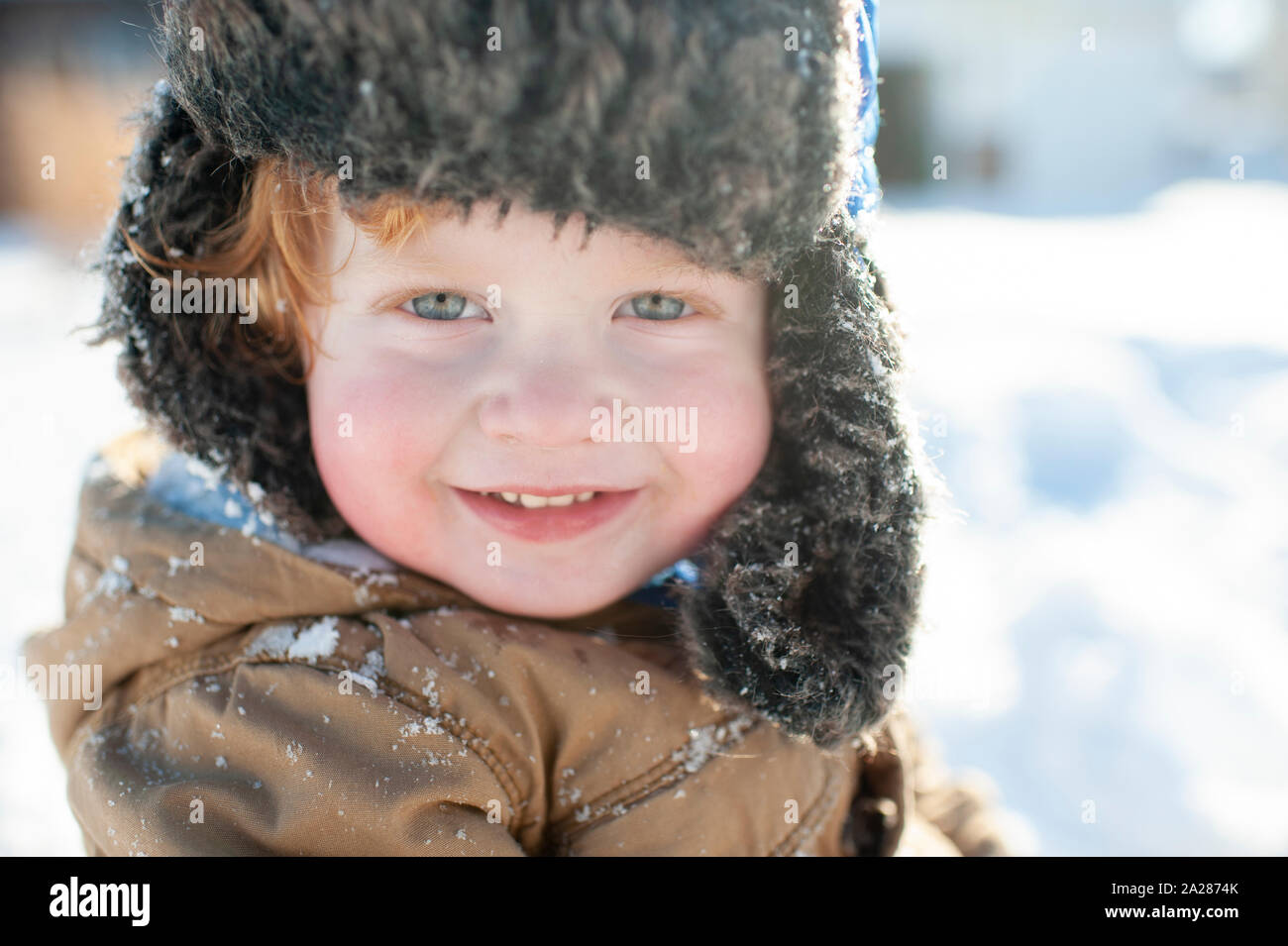 Up close of cute toddler in winter clothes and hat smiling in the snow Stock Photo