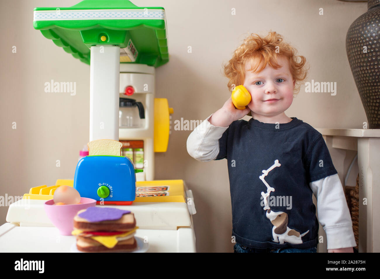 Toddler boy looking while answering phone in play kitchen at home Stock Photo
