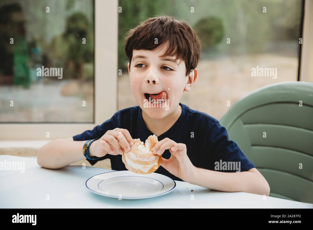 Portrait of boy with cream donut licking cream off his cheek Stock Photo