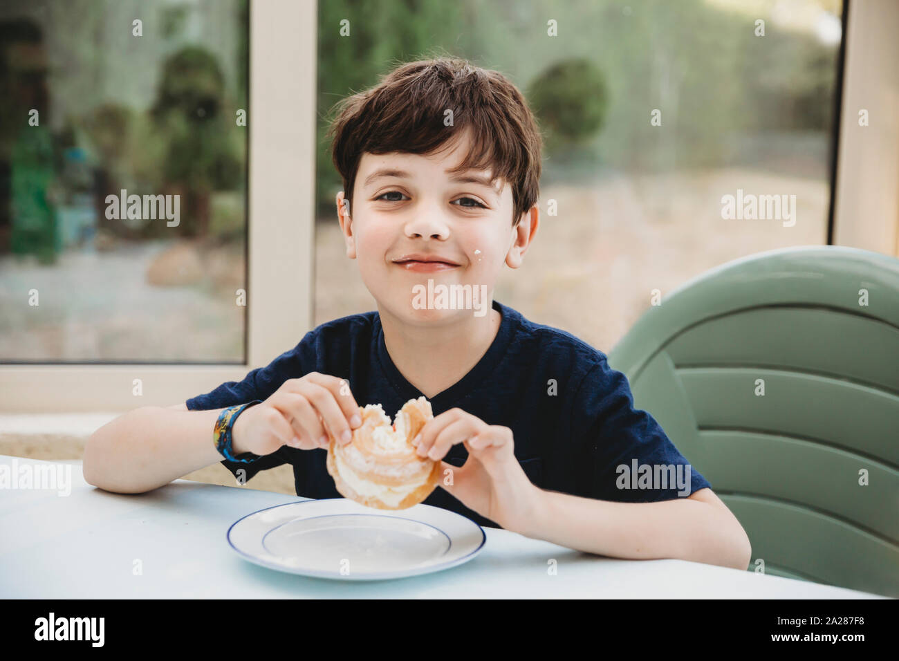 Portrait of boy enjoying cream donut with cream on his cheek Stock Photo