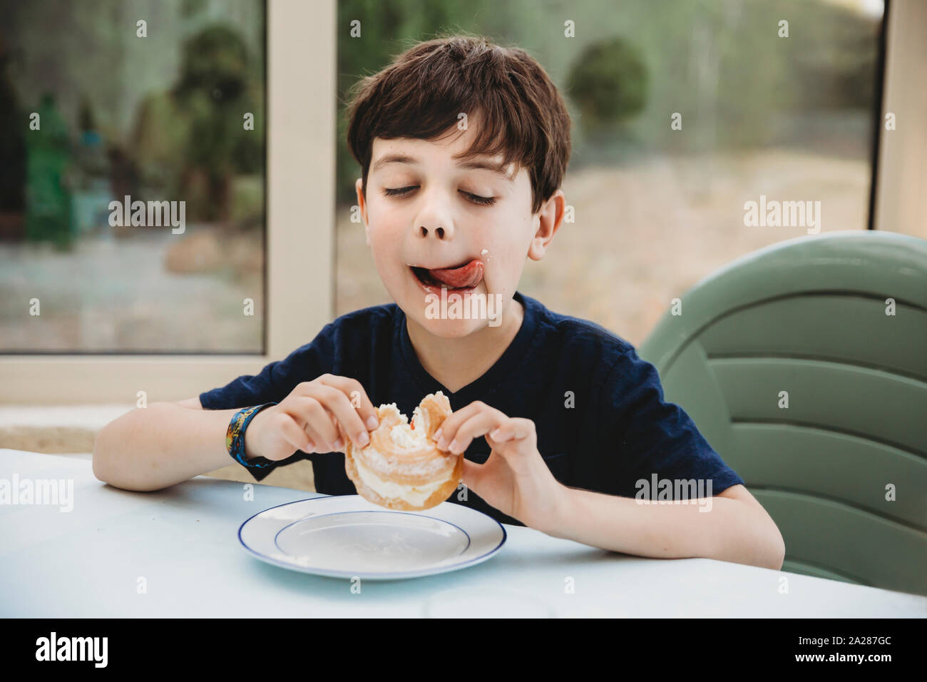 Portrait of boy with cream donut licking cream off his cheek Stock Photo