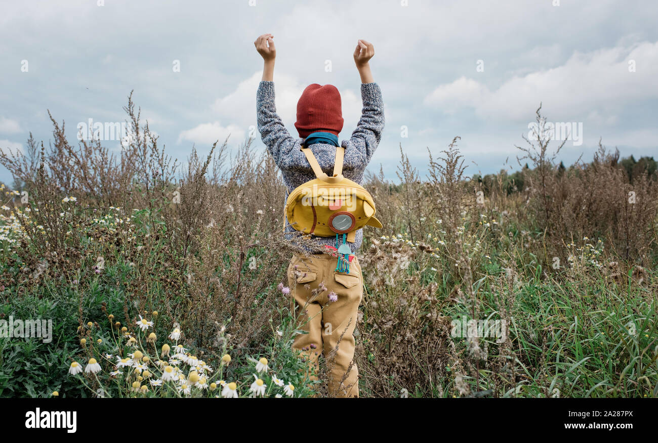 young school boy reaching up to the sky stood in a field of flowers Stock Photo