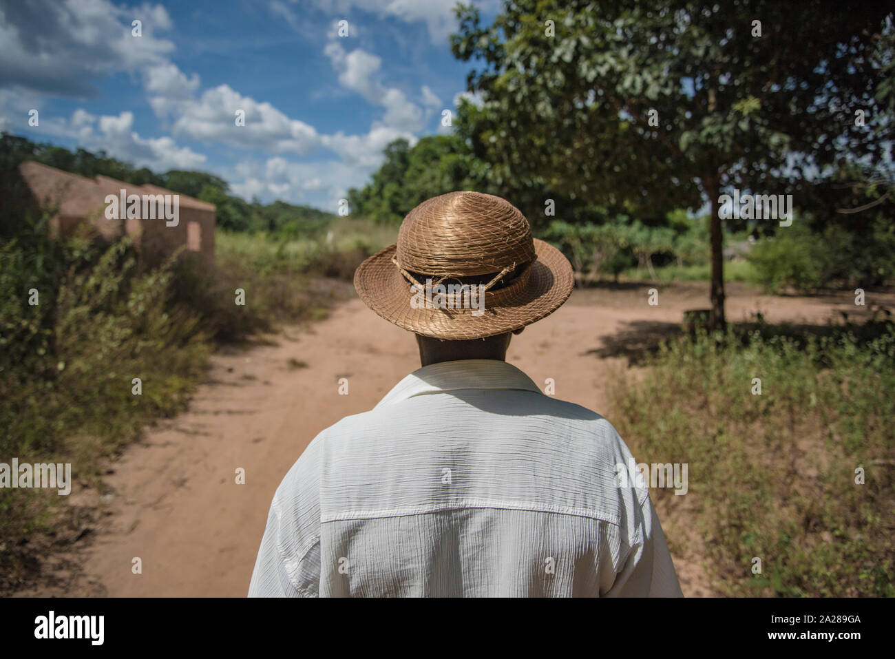 Farmer wearing wicker hat walking in a dirt road on countryside Stock Photo