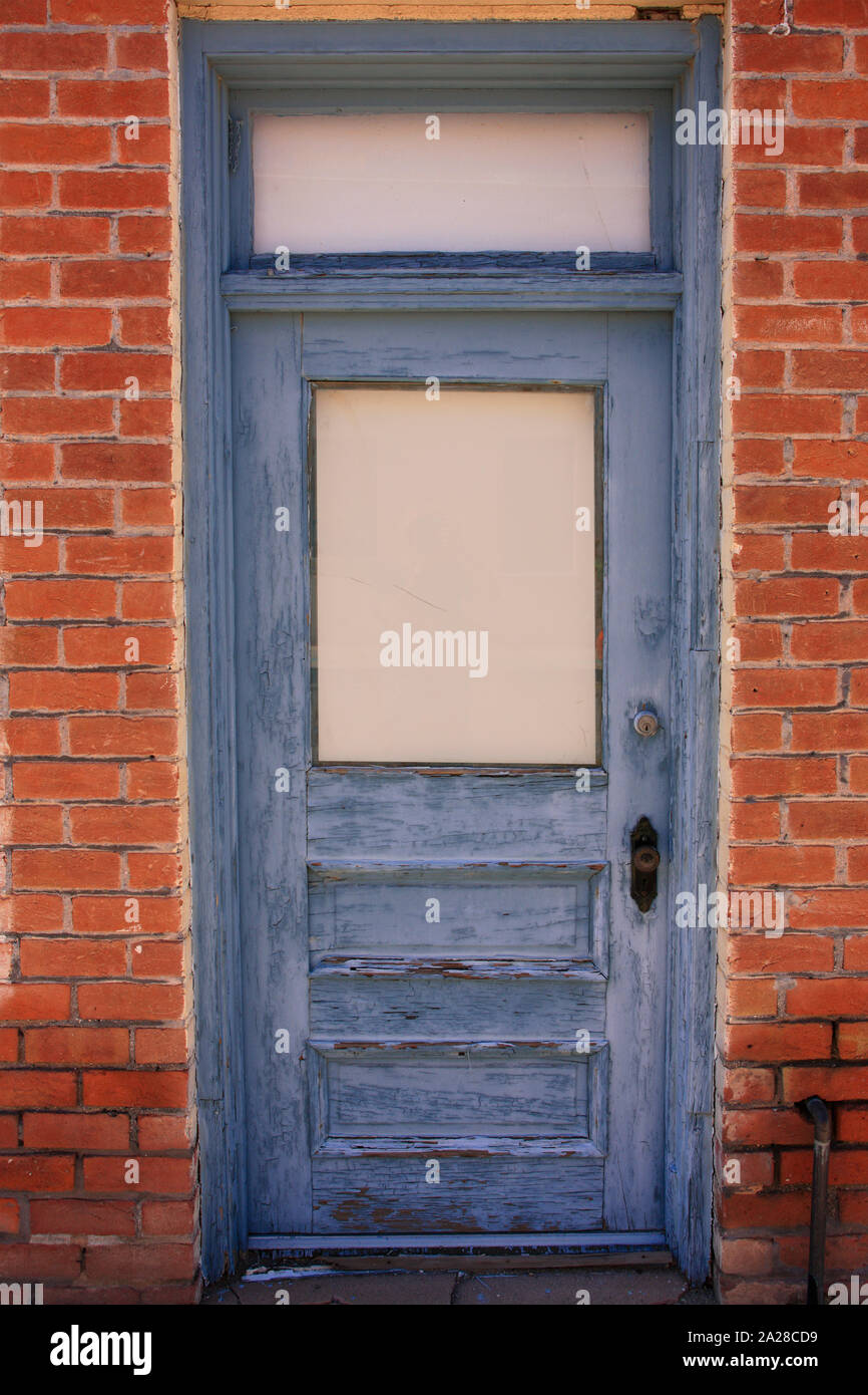 Distressed grey painted door set back in a red brick building doorway Stock Photo