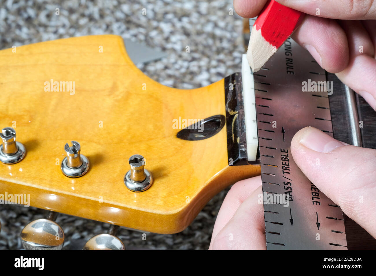 A guitar technician or tech measuring a piece of whalebone to make a new nut at the top of the fret board using a steel ruler Stock Photo