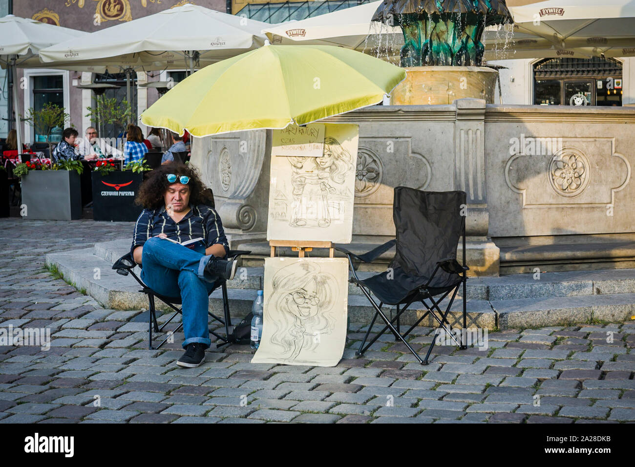 Caricature artist reading a book waiting for a customer. Stock Photo