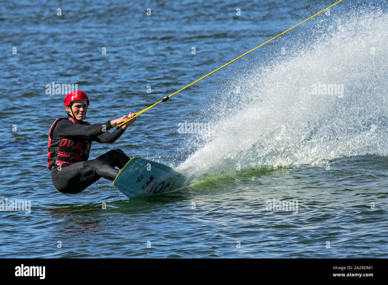 Wakeboarder / rider riding wakeboard towed by electrically-driven cable at cable ski course / wakeboard park Stock Photo
