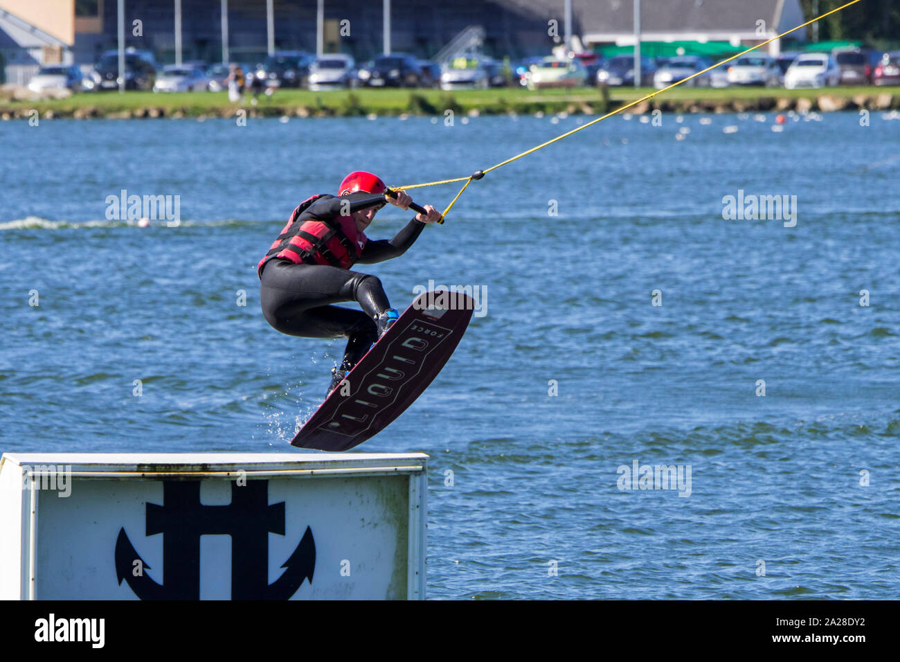 Wakeboarder / rider towed by electrically-driven cable jumping over ramp at cable ski course / wakeboard park Stock Photo