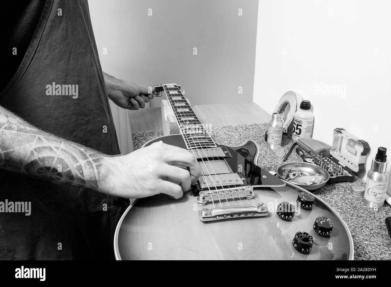 A guitar technician or tech tuning a re strung Gibson electric guitar in his workshop. He's tuning the tuning post whilst plucking the string Stock Photo