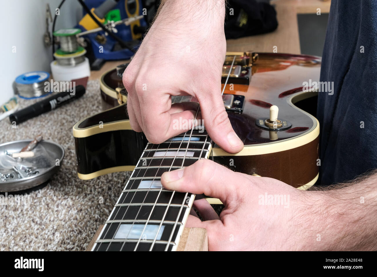 A guitar technician or tech, re stringing a Gibson guitar in his