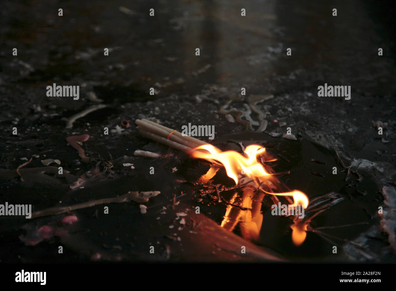 Reflection of the flame of a bunch of ritual wax candles in a puddle on ...