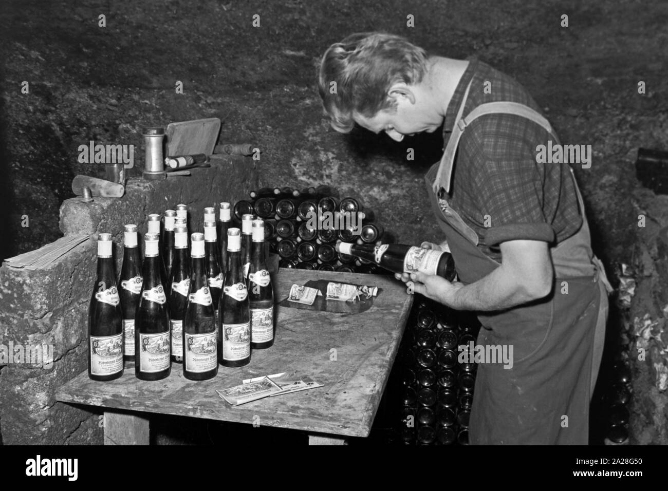 Kleben der Etiketten auf Weinflaschen in einem Weinkeller in Kröv, Deutschland 1968. Sticking the bottle labels on bottles in a wine cellar at Kroev, Germany 1968. Stock Photo