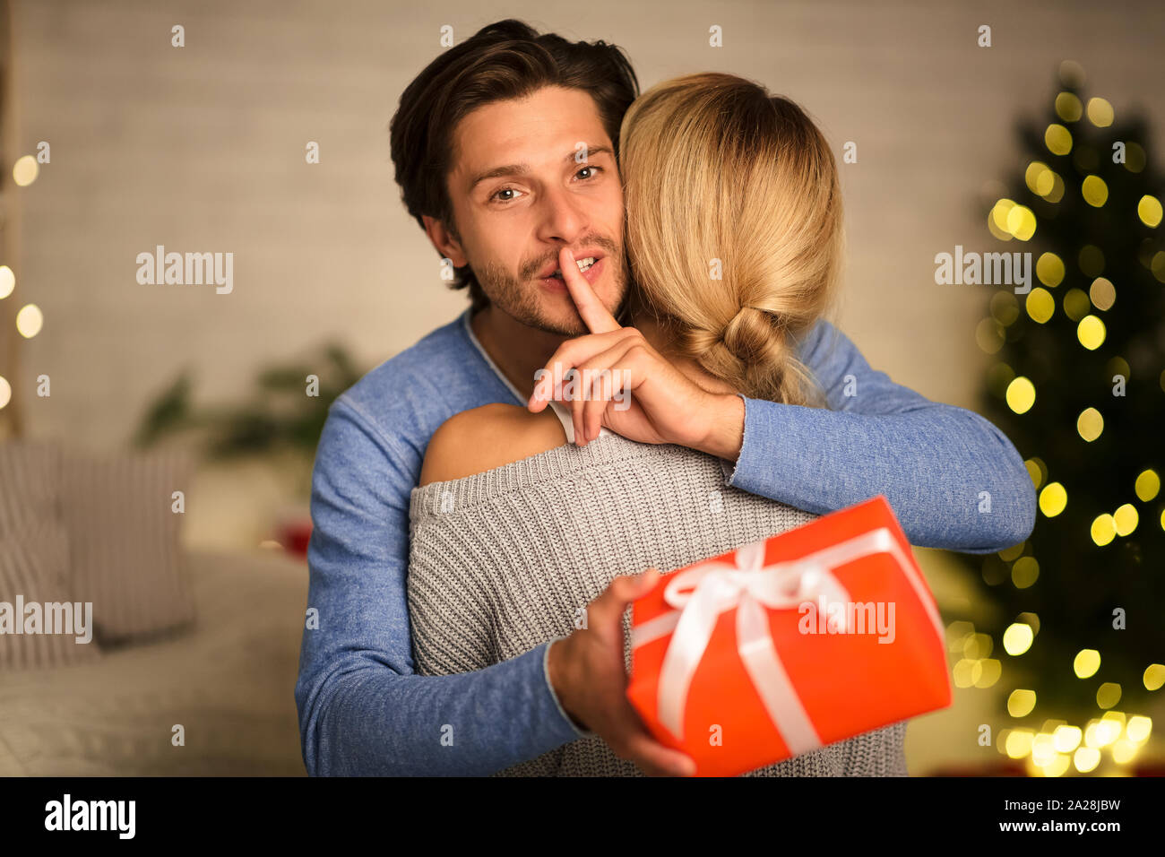 New Year surprise. Man making silence gesture and embracing woman Stock Photo