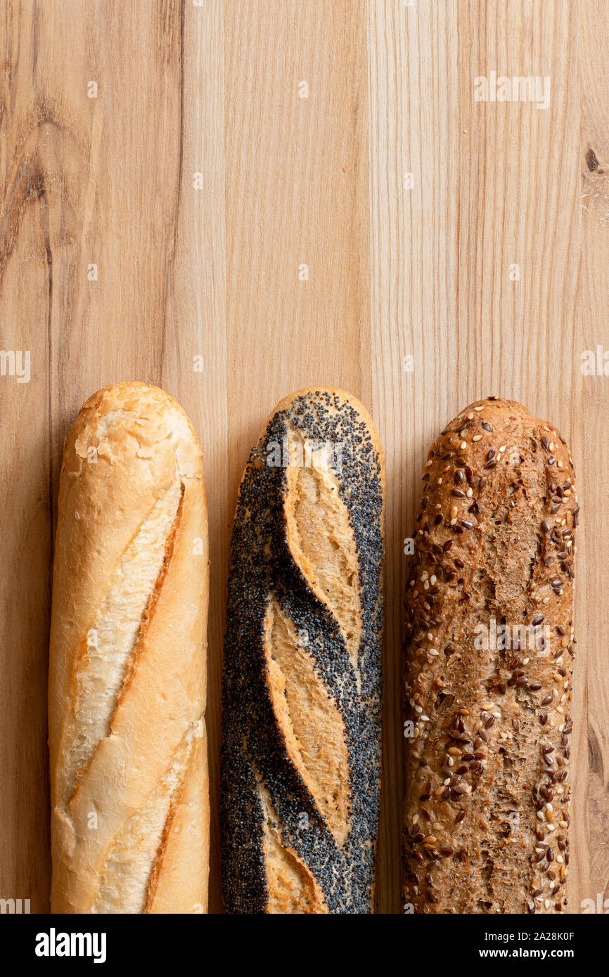 Three traditional baguettes on light wood. Plain, whole wheat and