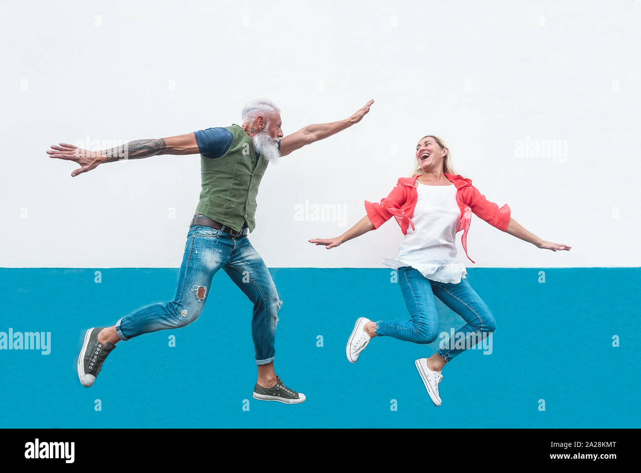 Happy seniors crazy couple jumping together outdoor - Mature trendy people having fun celebrating and dancing outside Stock Photo