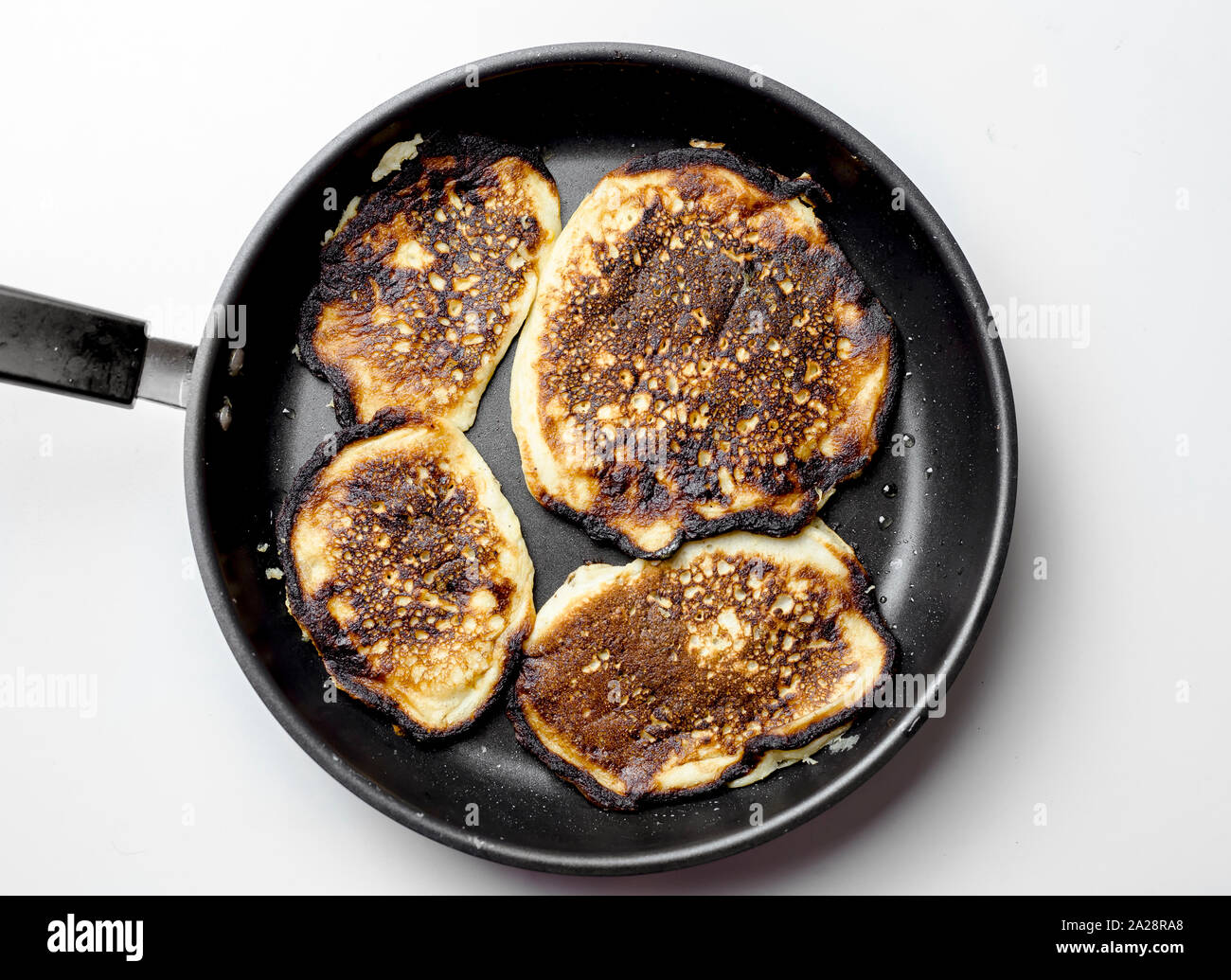 Cooking failed, burnt pancakes on a black pan, one pancake on a spatula. Stock Photo