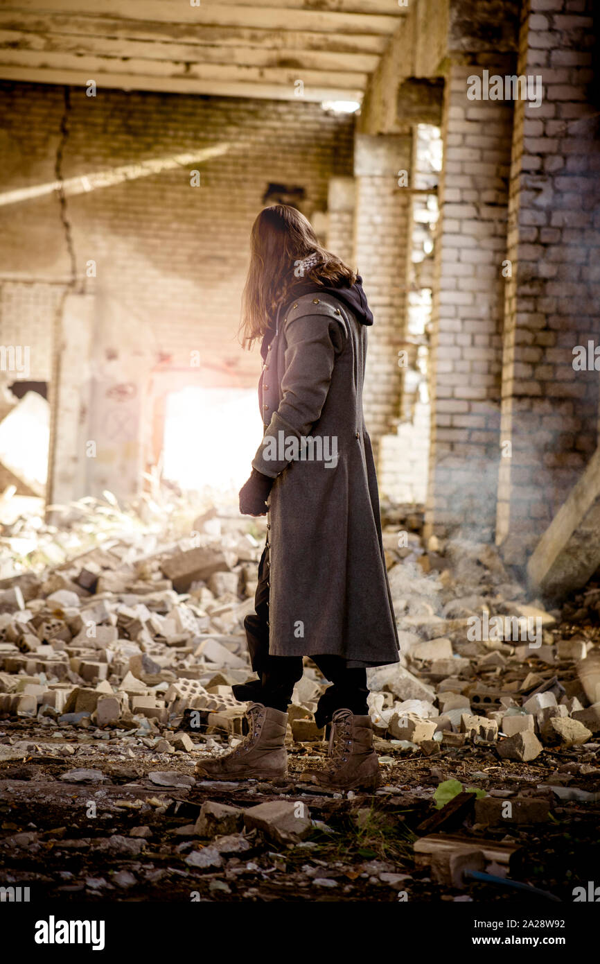 Young man standing in the ruins post apocalypse on earth, light shines from back, smoke on background. Stock Photo