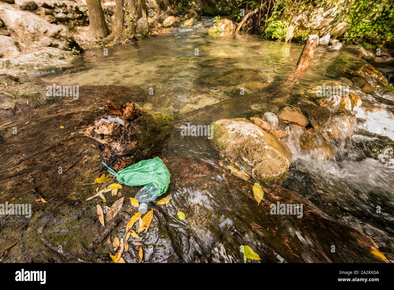 Garbage in an abandoned plastic bag on the bank of a river of clean water. Concepts of environmental damage and recycling of plastic containers. Stock Photo