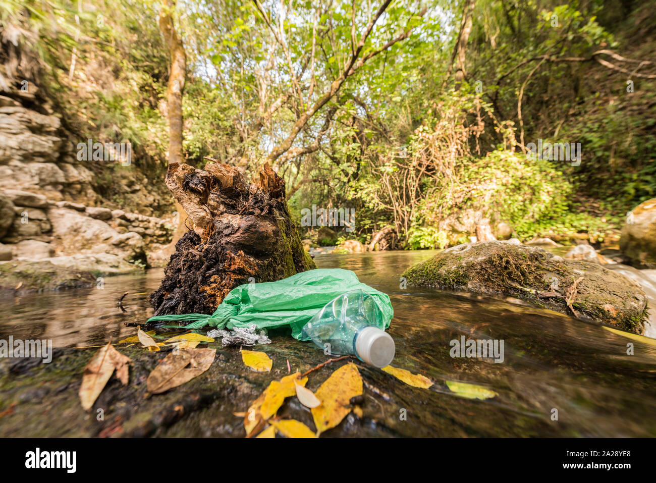 Garbage in an abandoned plastic bag on the bank of a river of clean water. Concepts of environmental damage and recycling of plastic containers. Stock Photo