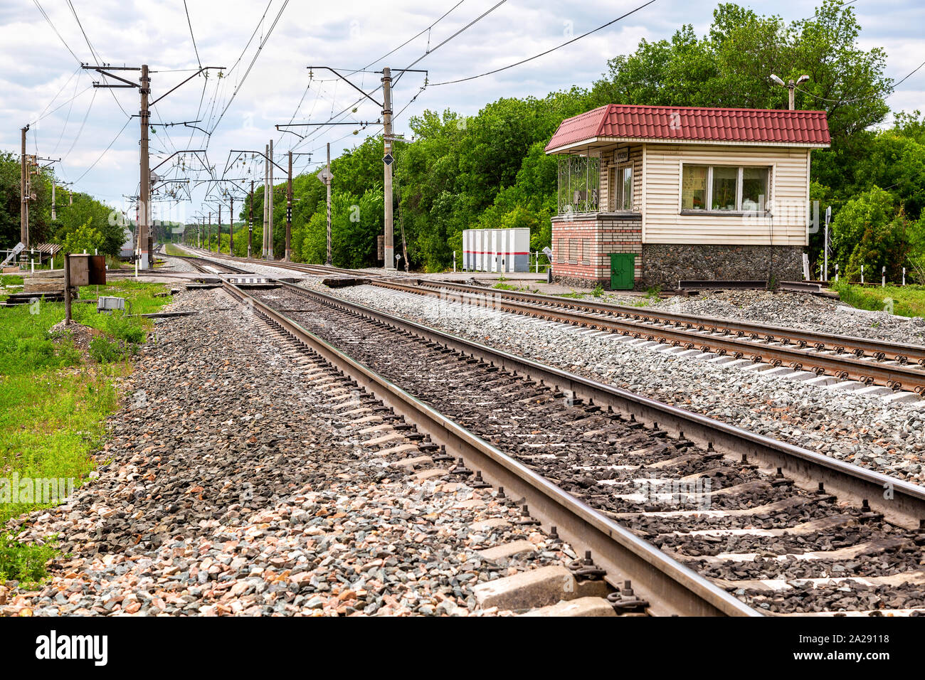 Double track electrified railway line with railway crossing in summer