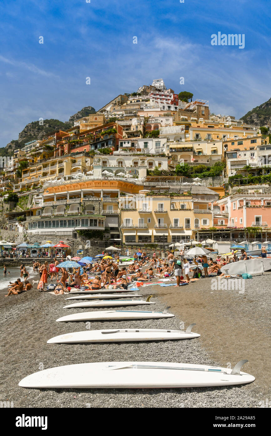 POSITANO, ITALY - AUGUST 2019: Surf boards and people on the beach in Positano. In the background are the coloured buildings of the town. Stock Photo
