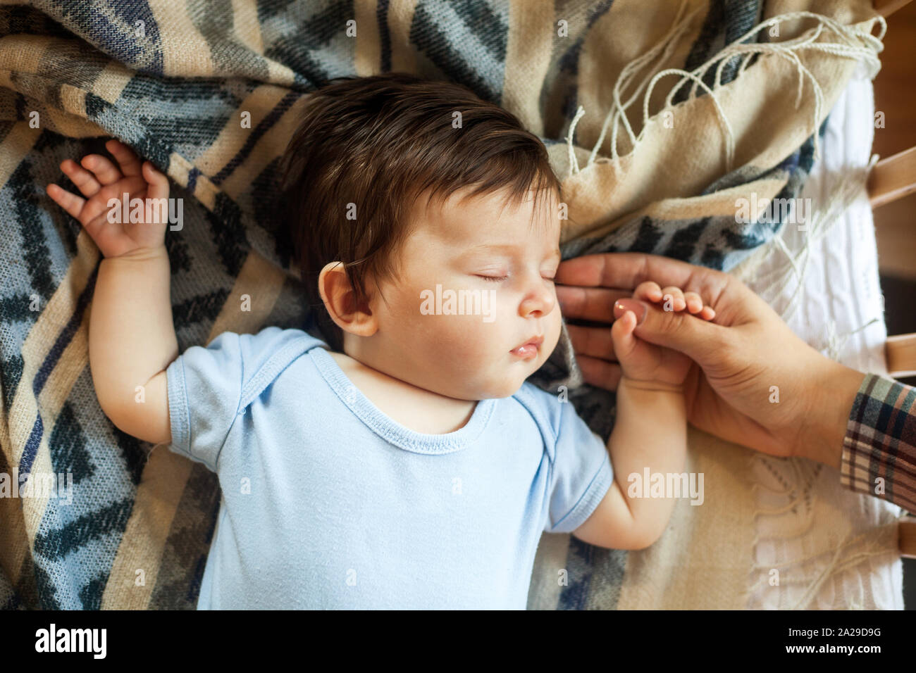 Little baby sleeping calm in bed at home, mother holding the hand, blue