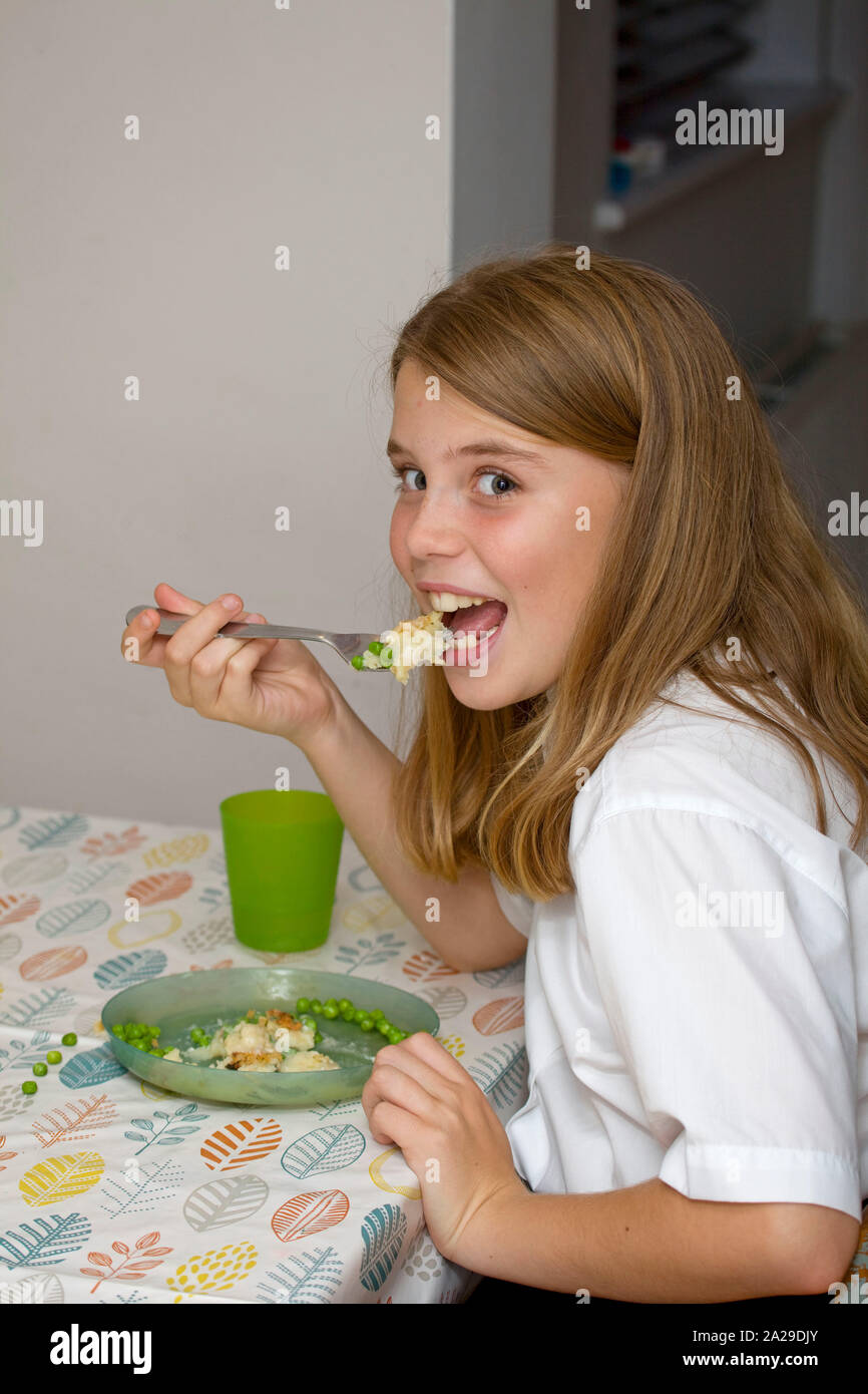 11 year old girl eating fish pie at the kitchen table Stock Photo