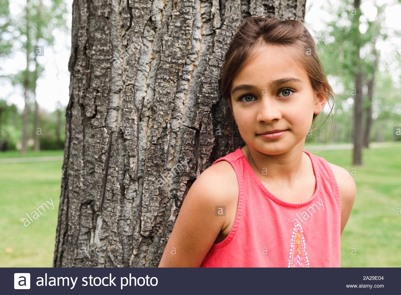 Portrait of young girl leaning against tree and looking at camera Stock Photo