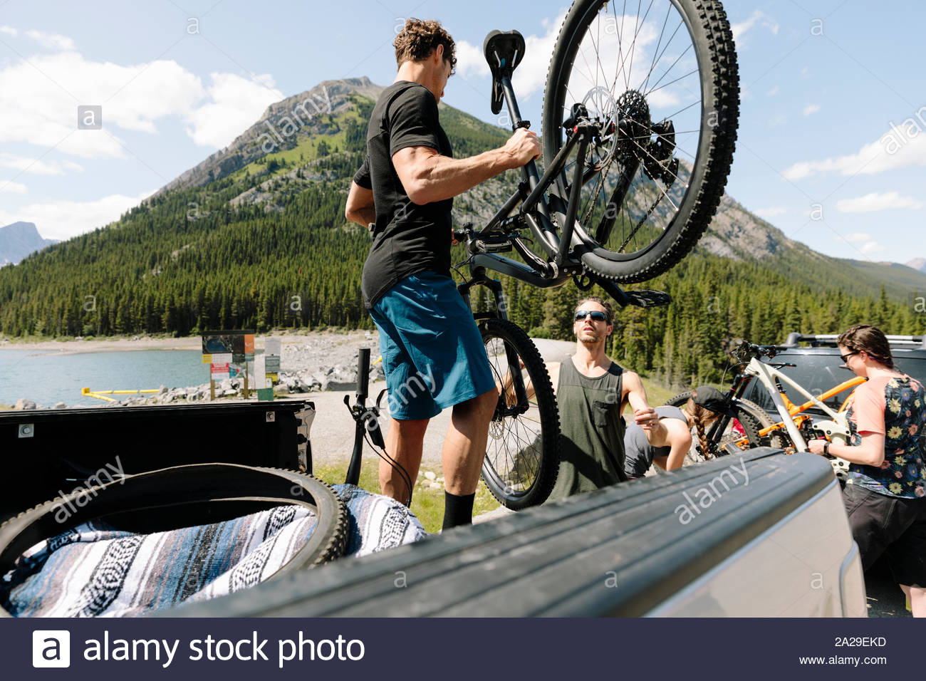 Friends unloading mountain bikes from pickup truck at sunny lakeside