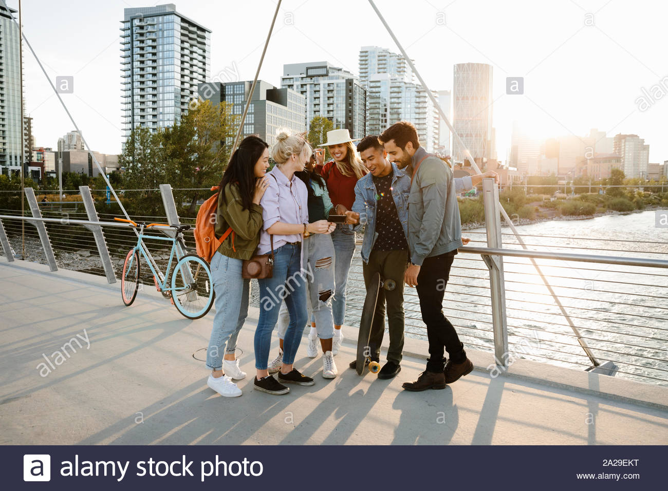 Happy young adult friends using digital tablet on sunny, urban bridge Stock Photo