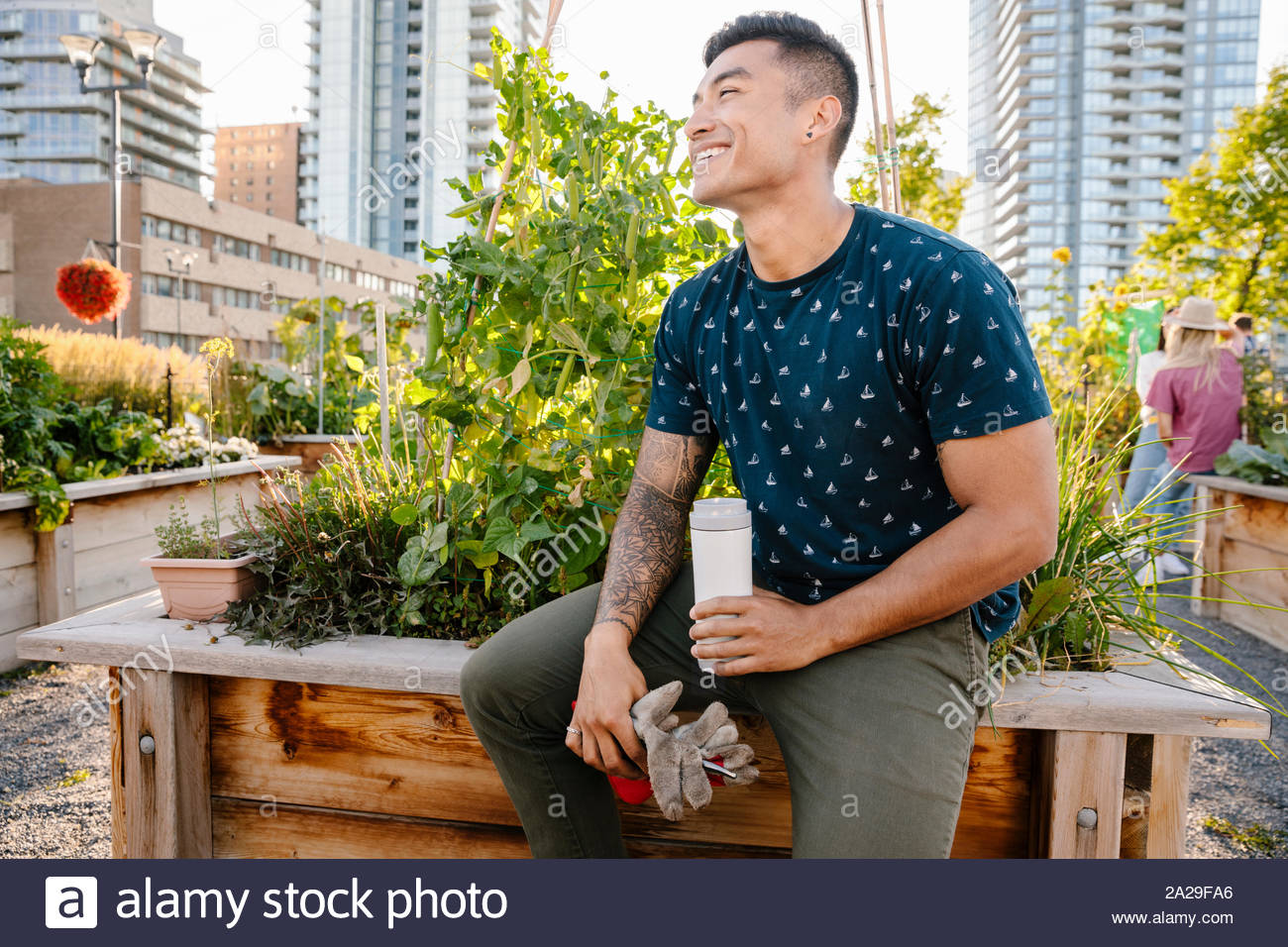 Happy young man resting, drinking water in urban community garden Stock Photo
