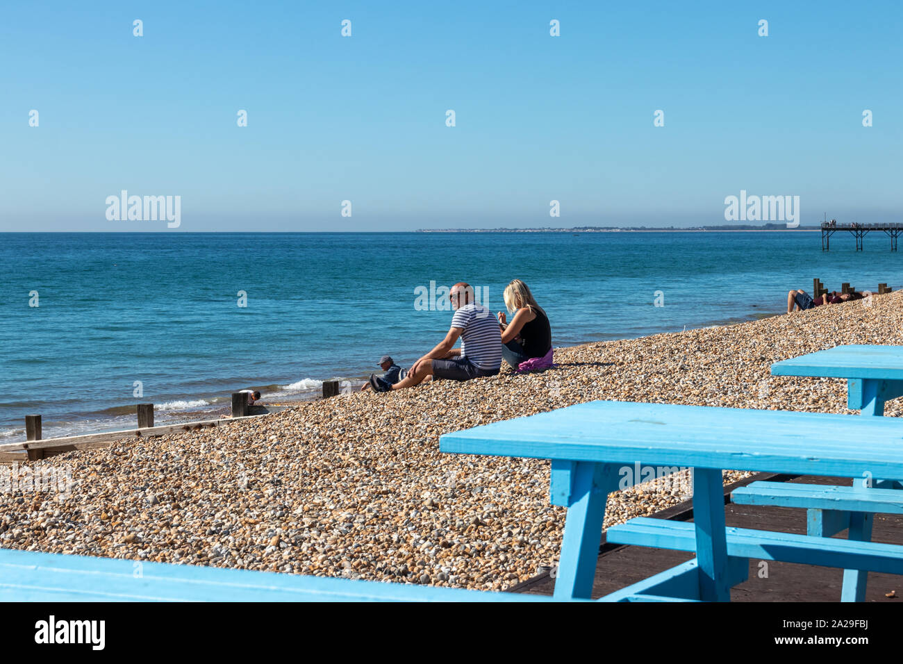 A middle aged couple sat on a British pebble beach enjoying the sunshine on a summers day Stock Photo