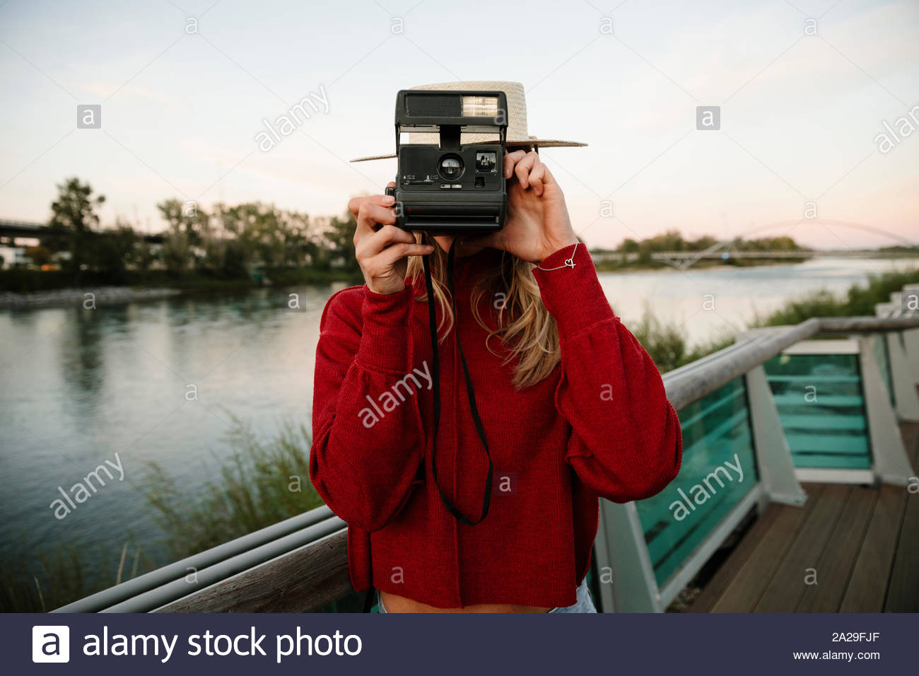 Portrait young woman using instant camera at waterfront Stock Photo